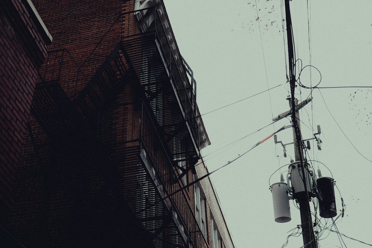 A moody urban scene with fire escapes and power lines on a rainy day.